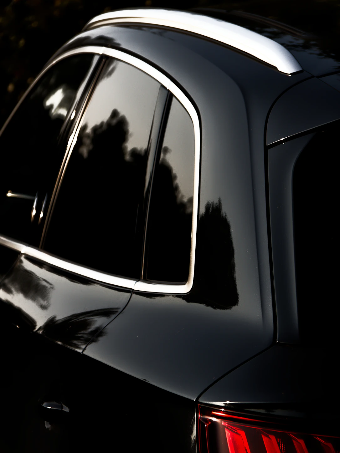 Dark tinted rear glass on a black SUV showing only the trees reflected in it