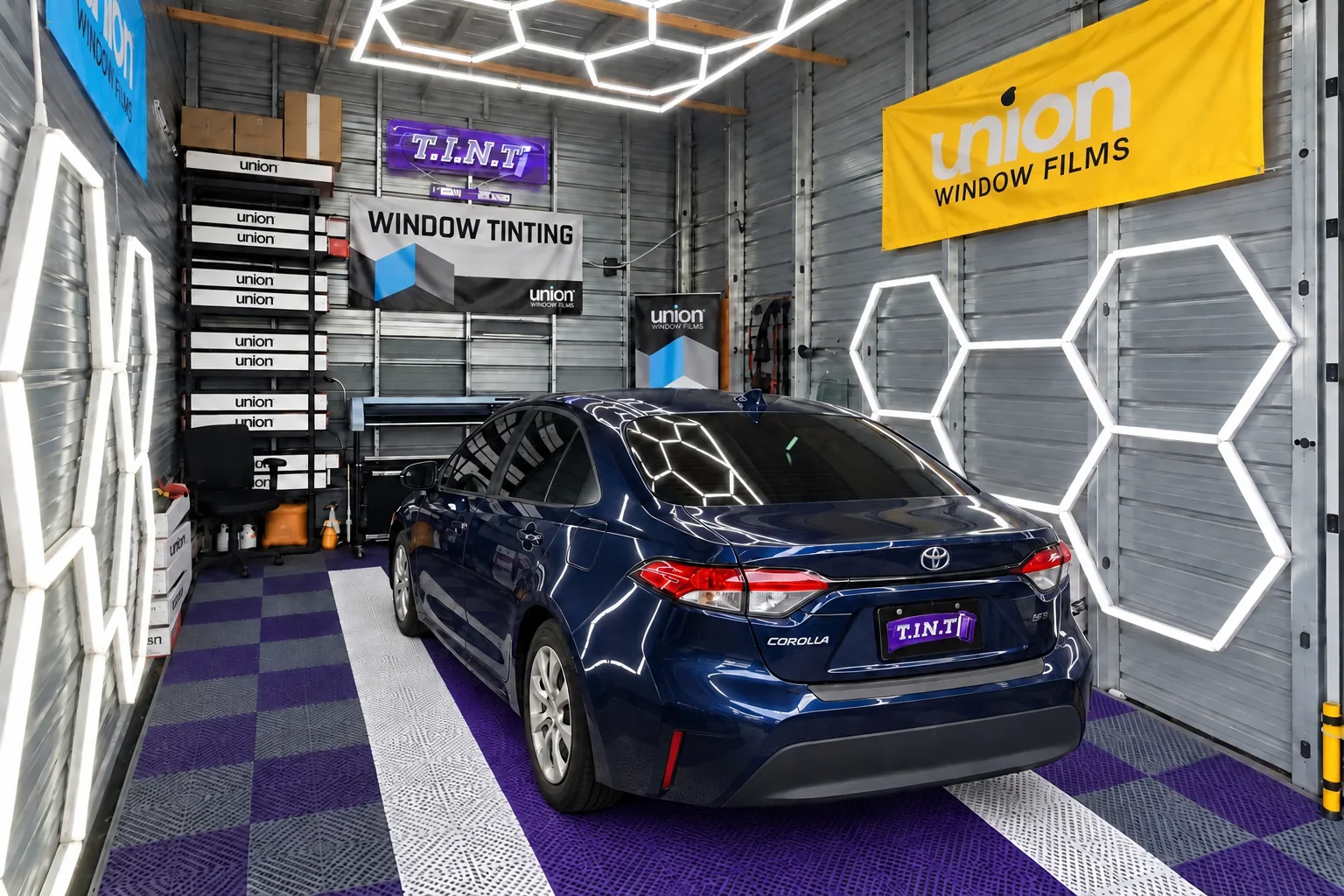 A navy Toyota Corolla with new window tint in the T.I.N.T bay, on the purple and white floor