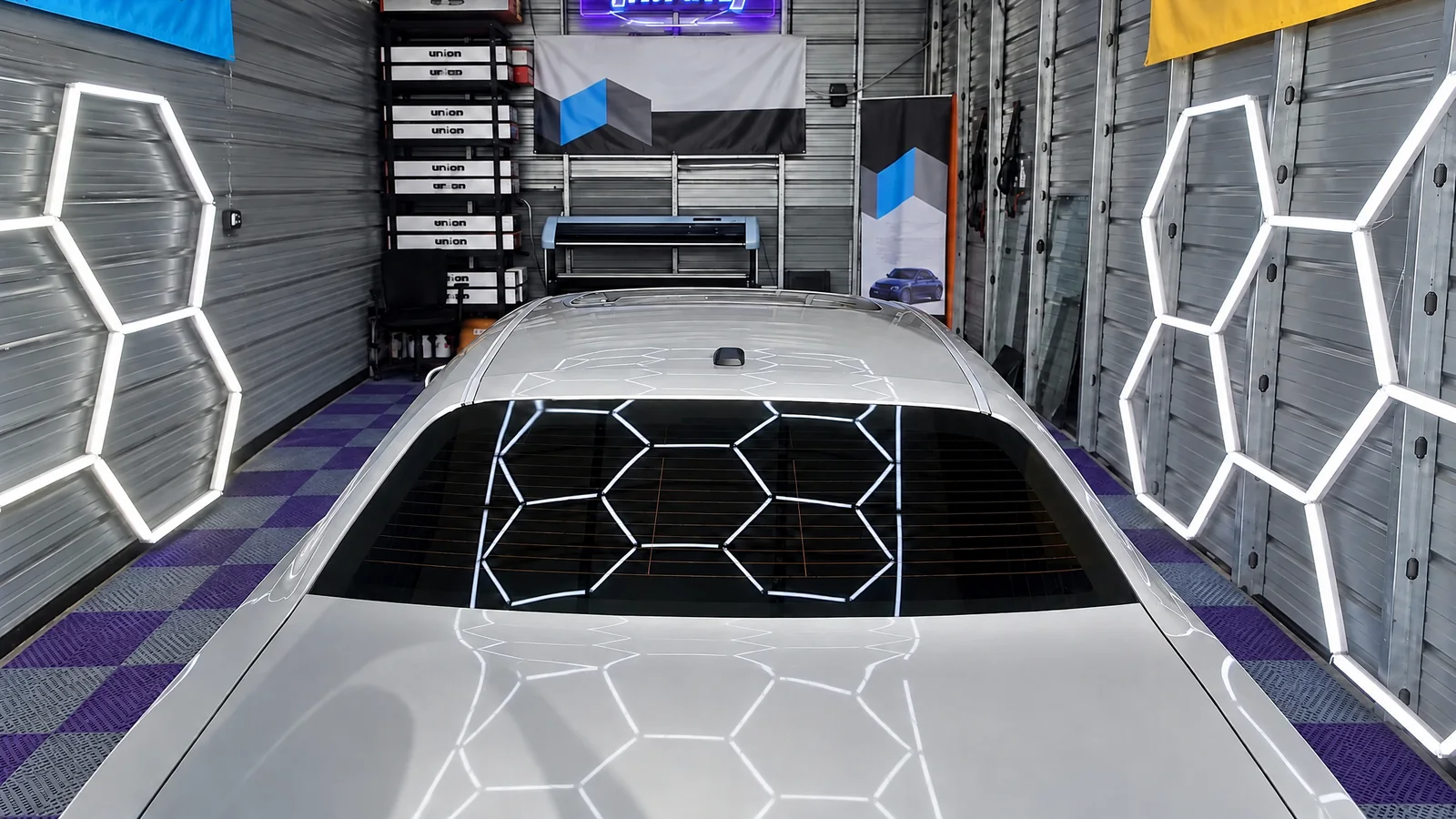 A silver car in the T.I.N.T bay in Tacoma, its rear window freshly tinted, hexagon lights on the walls