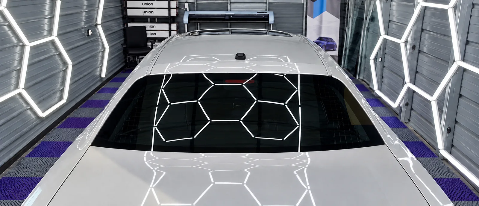 The silver car’s tinted rear window in the bay, the hexagon lights reflected in it