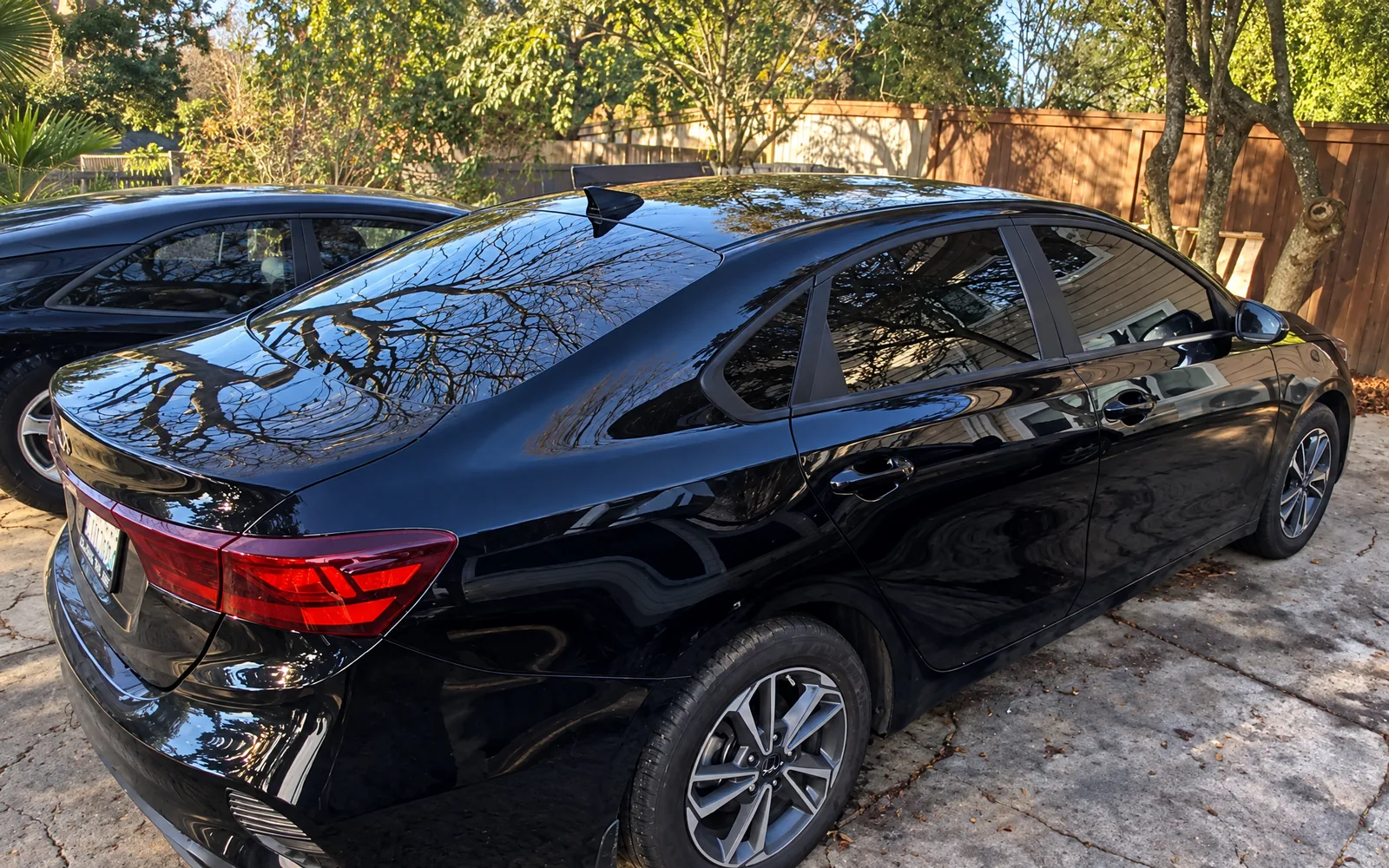 A black Kia sedan with tinted windows on a customer’s driveway